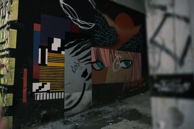 Graffiti art on a dark wall: faces, geometric shapes, and colorful designs in an alleyway.