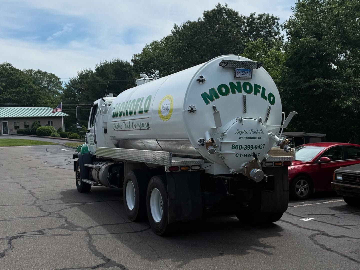 White Monoflo septic truck parked outdoors with green and red vehicles.