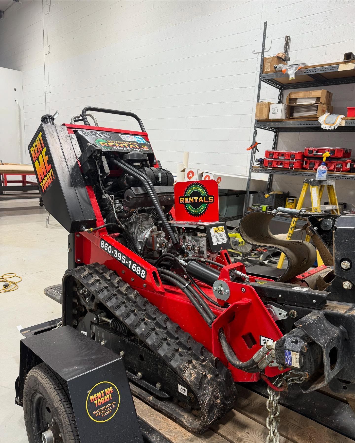 Red and black mini trencher on a trailer, indoors, with tools and shelves in the background.