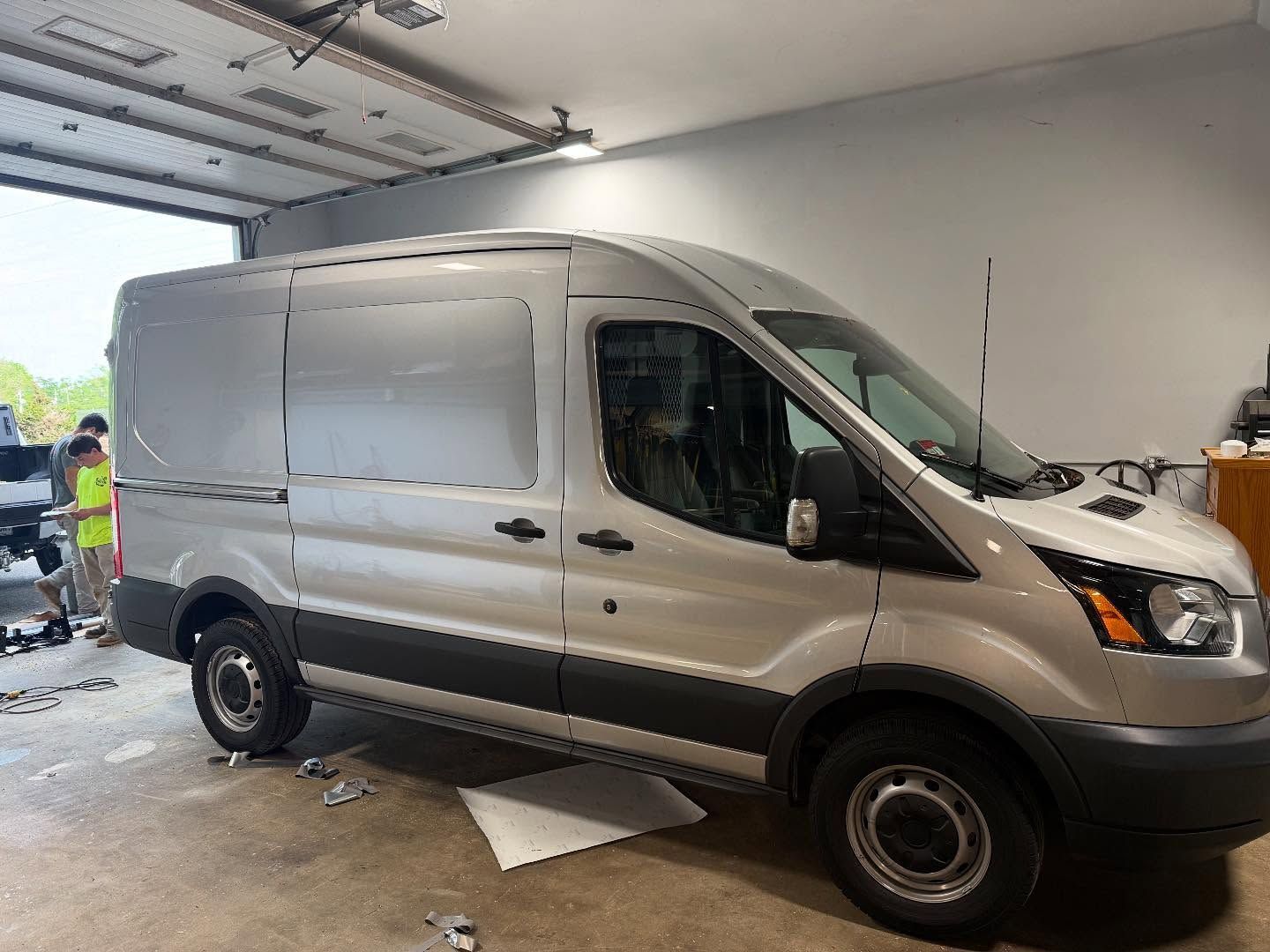Silver cargo van parked in a garage; two people in background.