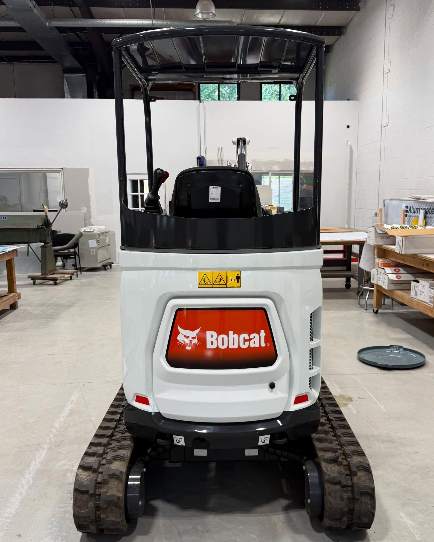 Bobcat excavator on tracks, white and black, indoors.