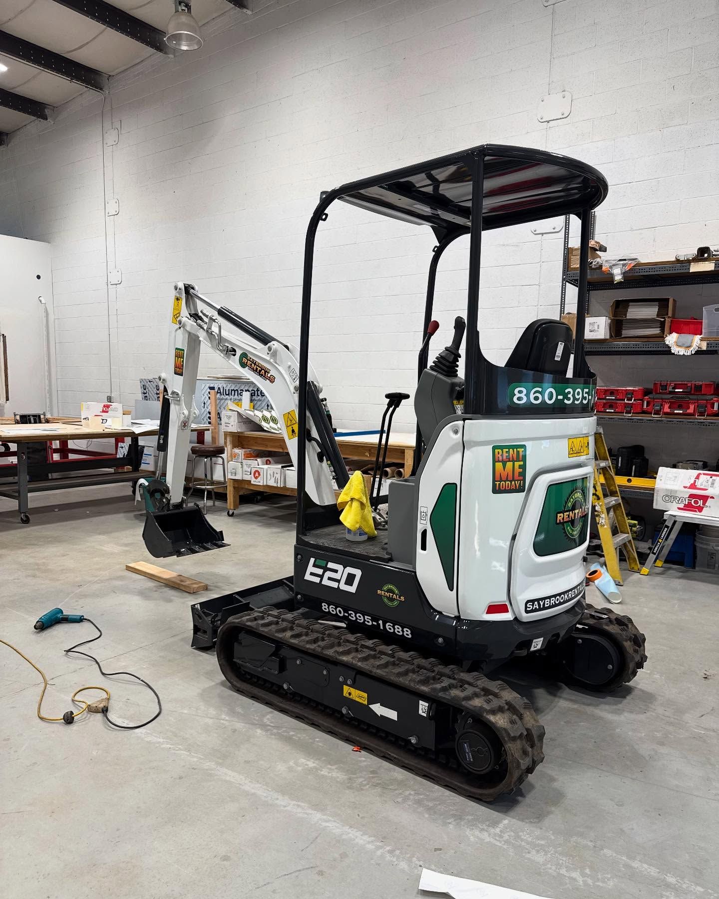 Small white and green Bobcat E20 excavator inside a warehouse.