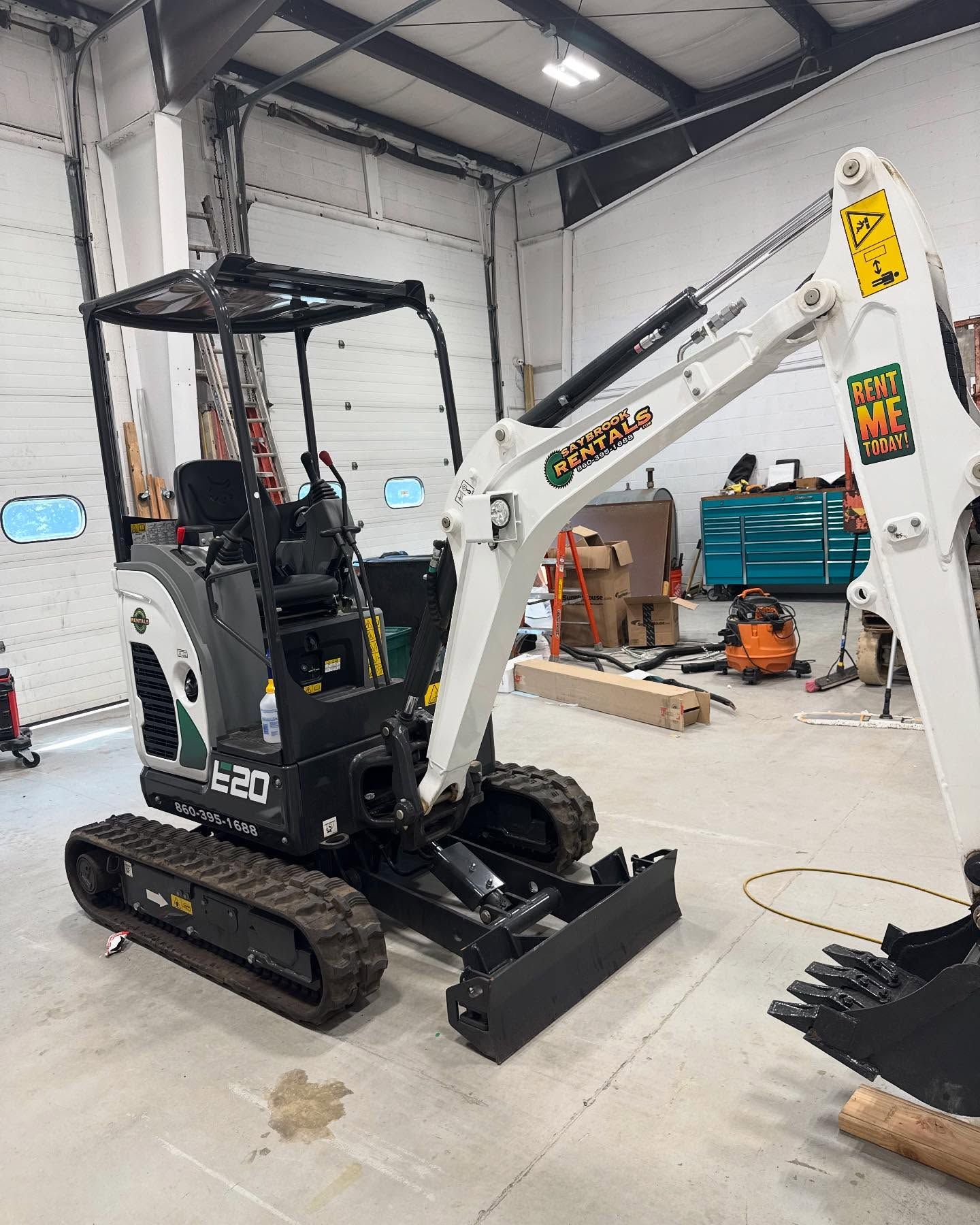 A small white and black excavator inside a garage, with the boom arm extended.