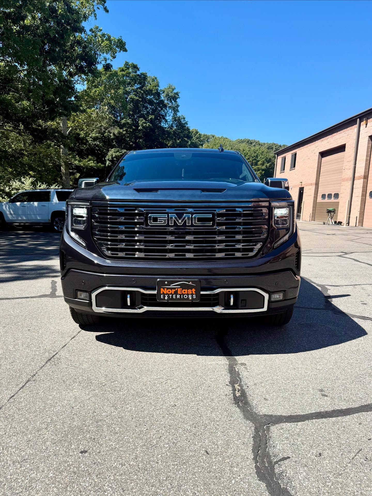 Black GMC Yukon Denali SUV parked on pavement. Bright sunny day.