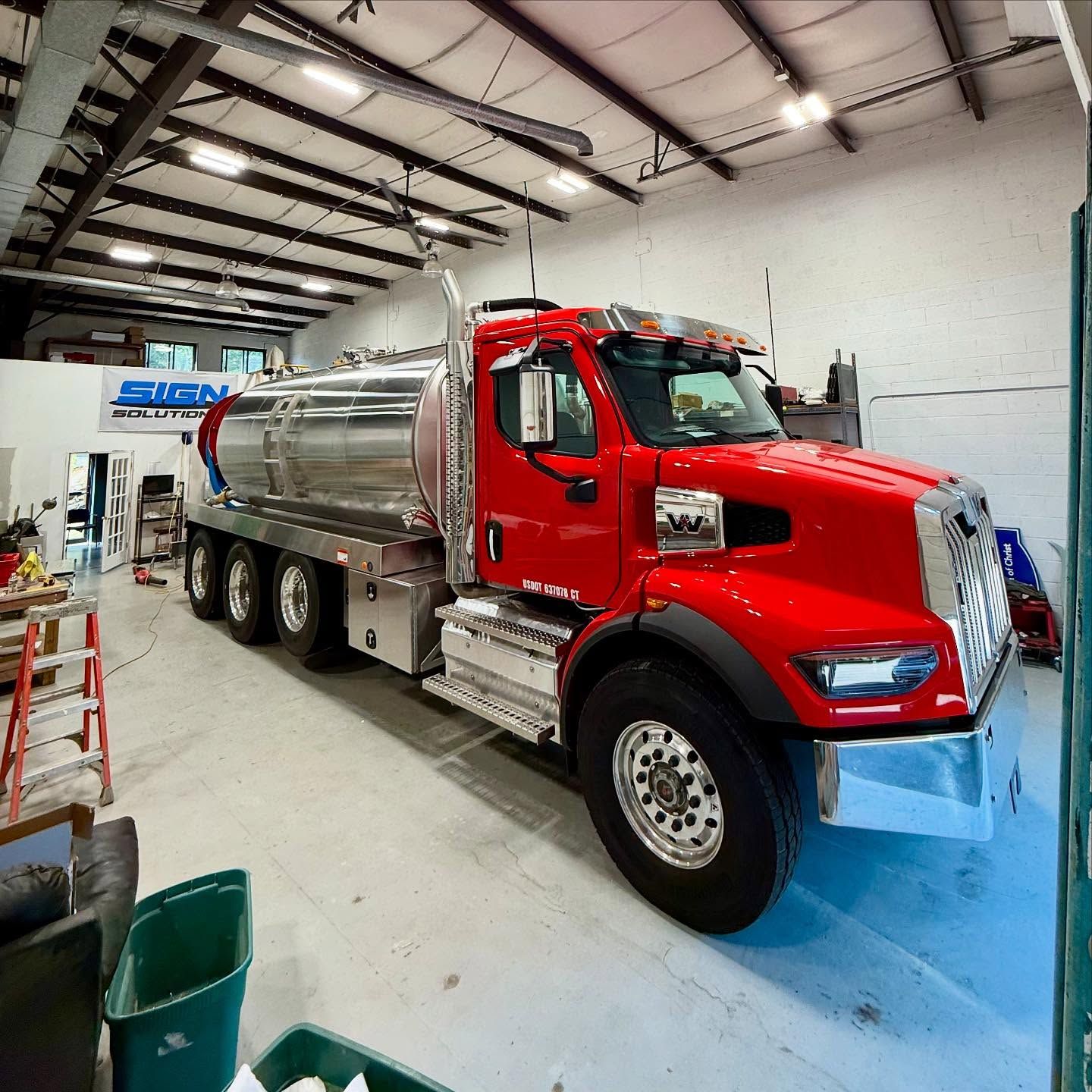 Red tanker truck parked inside a brightly lit garage with a sign for