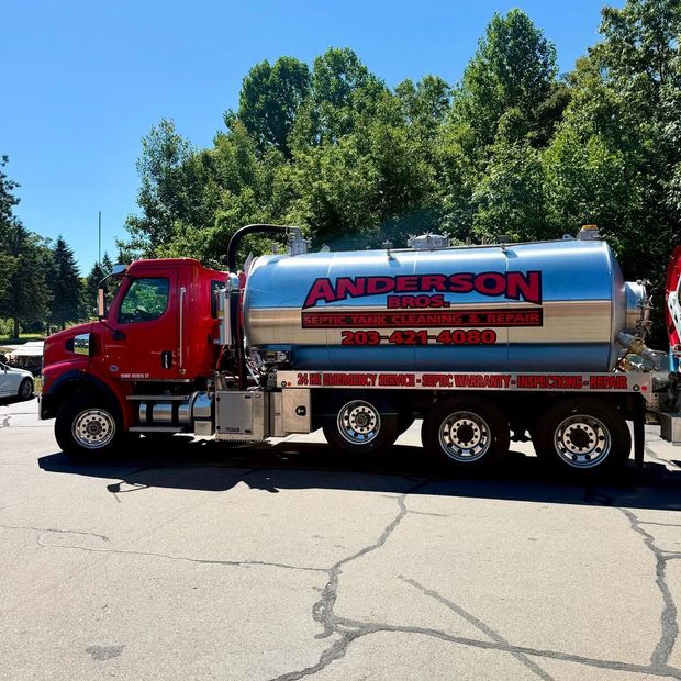 Red and silver Anderson Septic truck parked on cracked asphalt.