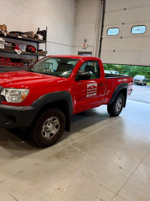 Red Toyota Tacoma truck parked inside a garage with the door partially open.