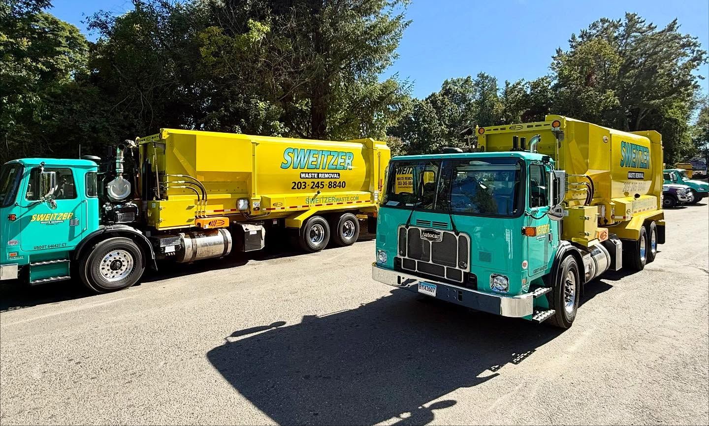 Two green and yellow trash trucks parked outdoors on a sunny day.