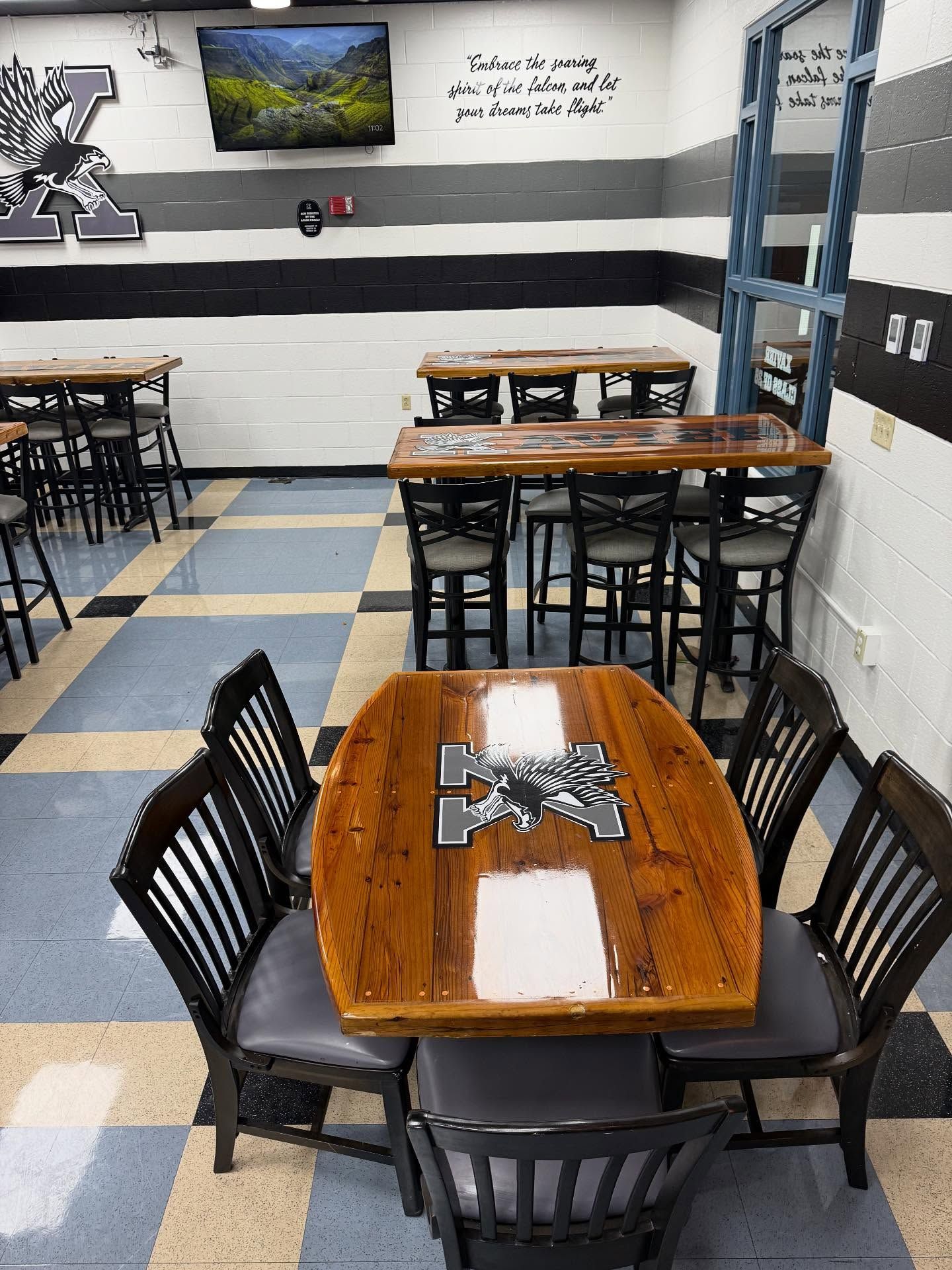 Restaurant with wood tables, checkered floor, black chairs. Wall art & a TV.