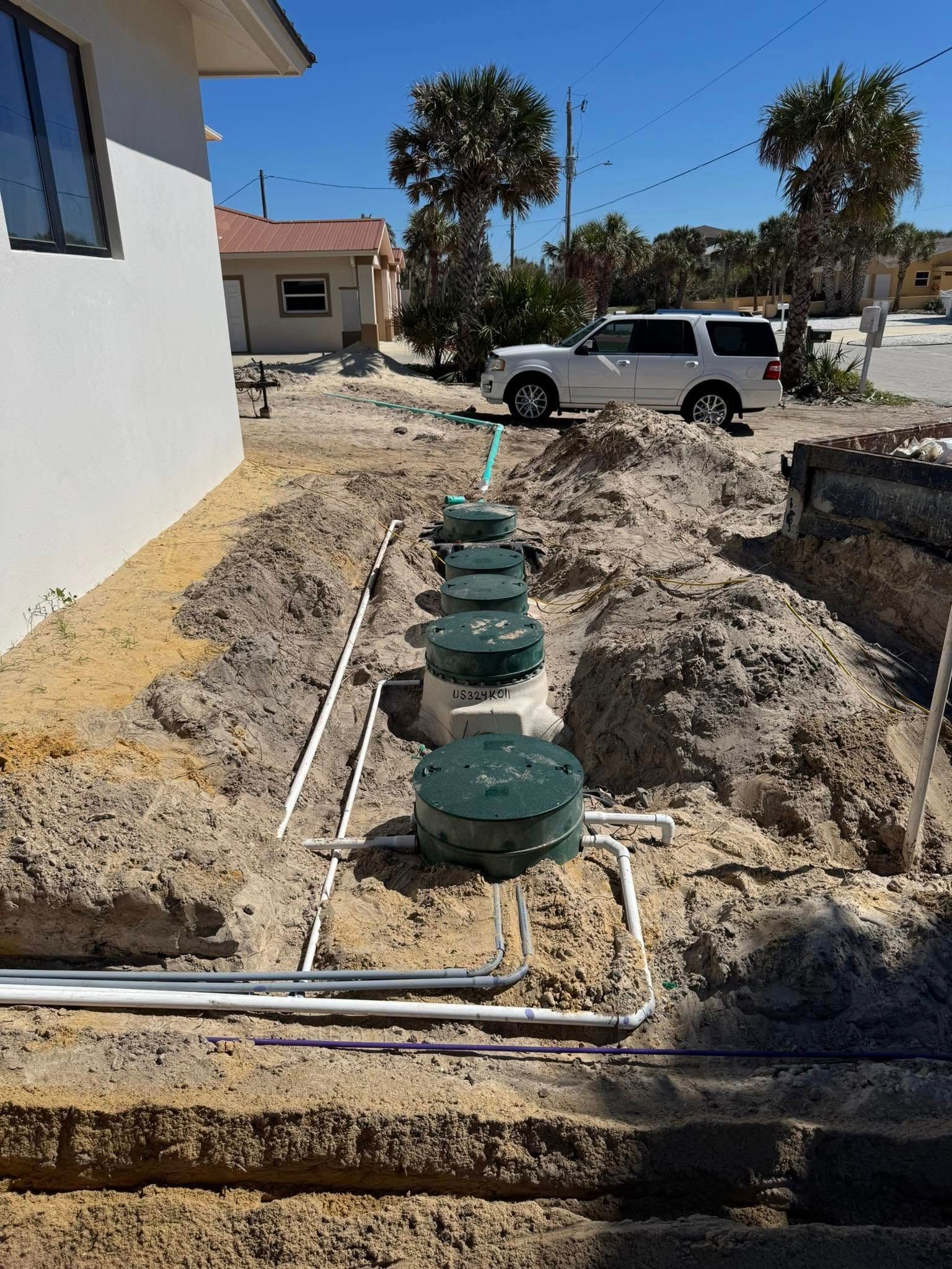 A row of septic tanks are sitting in the dirt in front of a house.