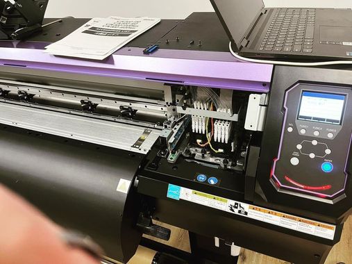 Large format printer with open access panel, a laptop, and control panel.