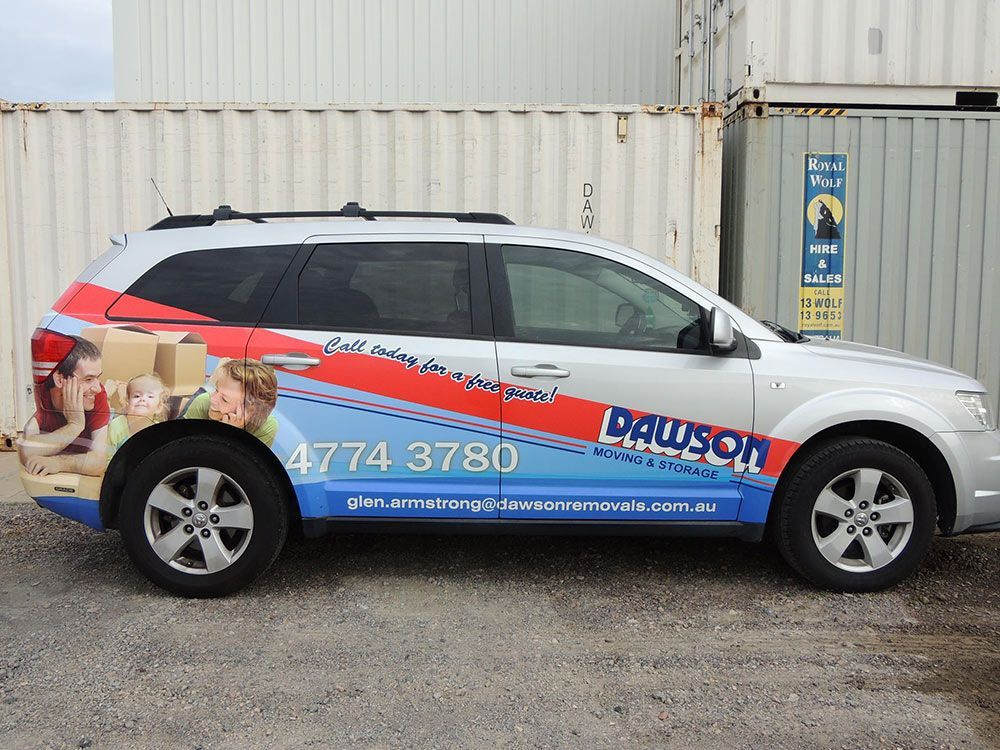 A White Suv With A Pause On The Side Is Parked In Front Of A Shipping Container — Dawson Moving & Storage NQ in Mount St John, QLD