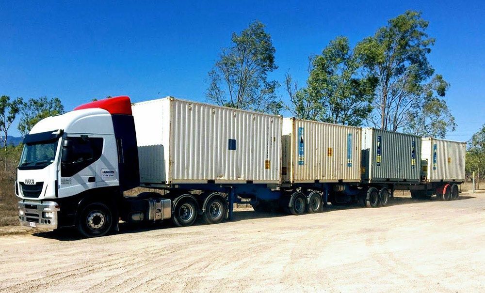 A Truck With A Trailer Full Of Shipping Containers Is Parked In A Dirt Lot — Dawson Moving & Storage NQ in Mount St John, QLD