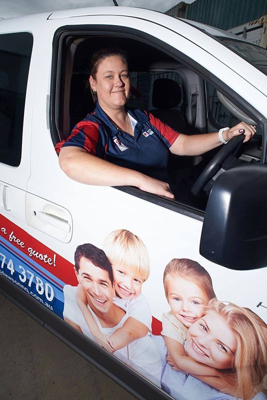 A Woman Is Sitting In The Driver's Seat Of A White Van With A Picture Of A Family On The Side — Dawson Moving & Storage NQ in Mount St John, QLD