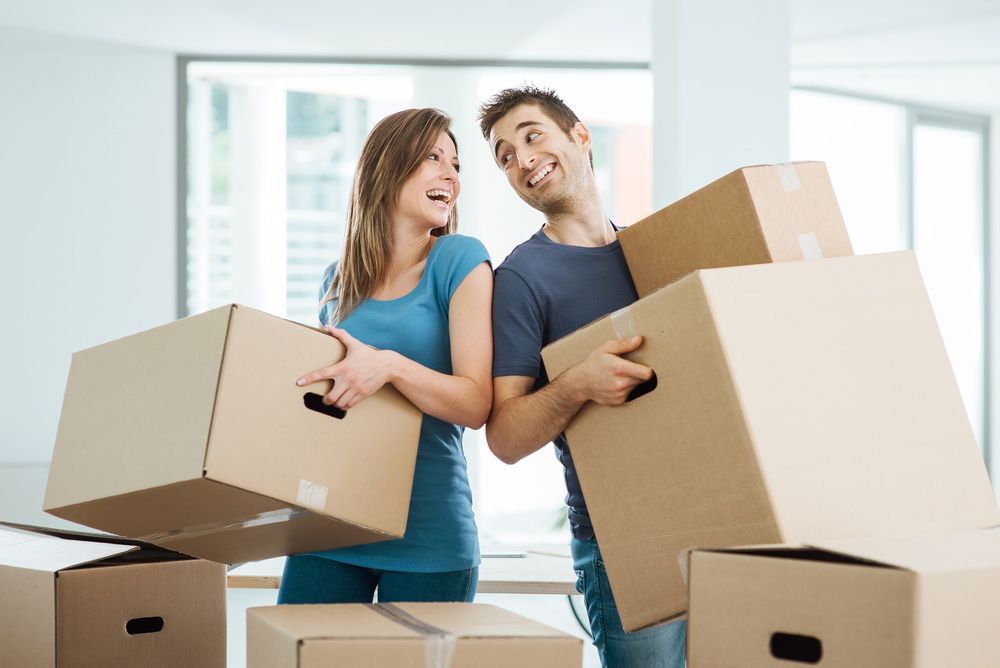 A Man And A Woman Are Holding Cardboard Boxes In Their Hands — Dawson Moving & Storage NQ in Canberra, ACT
