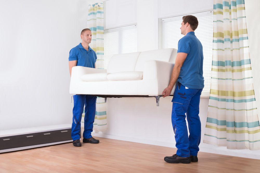 Two Men Are Carrying A White Couch In A Living Room — Dawson Moving & Storage NQ in Melbourne, VIC