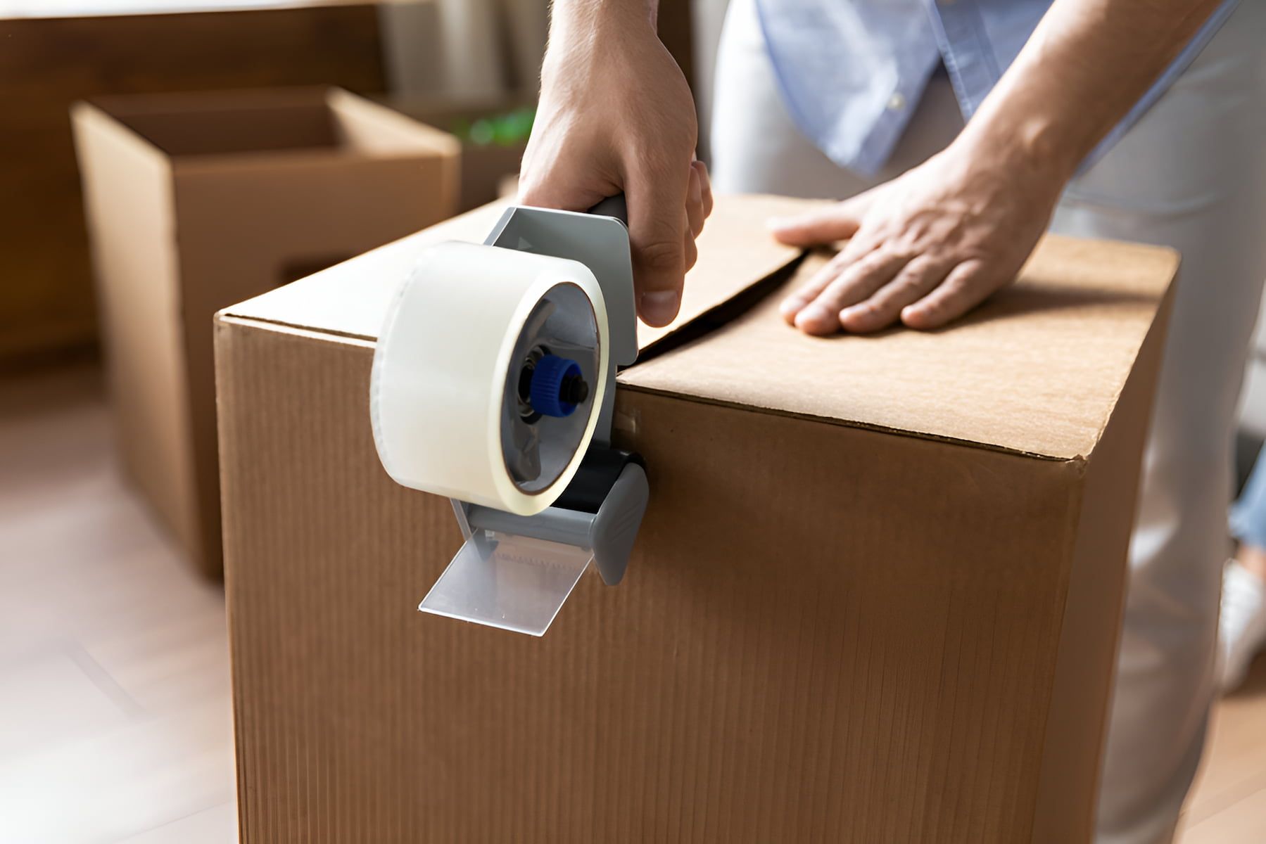 A Person Is Taping A Cardboard Box With Tape — Dawson Moving & Storage NQ in Mount St John, QLD