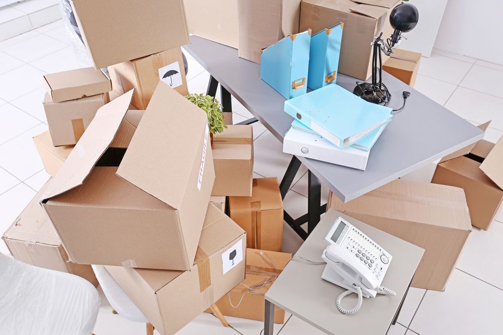 Packed moving boxes stacked around a desk with office items during home or office relocation process