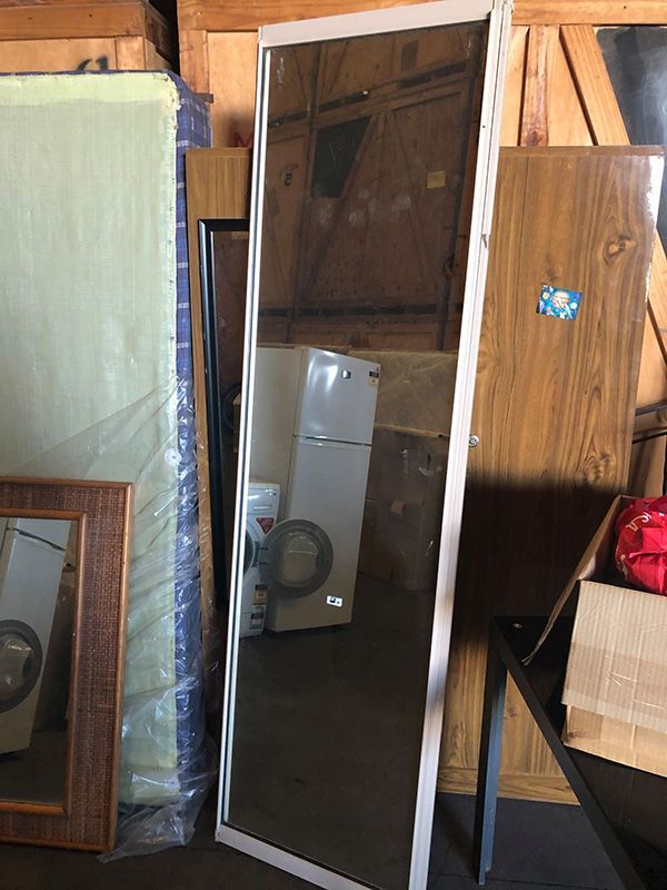A Full Length Mirror Is Sitting In A Warehouse Next To A Refrigerator — Dawson Moving & Storage NQ in Mackay, QLD