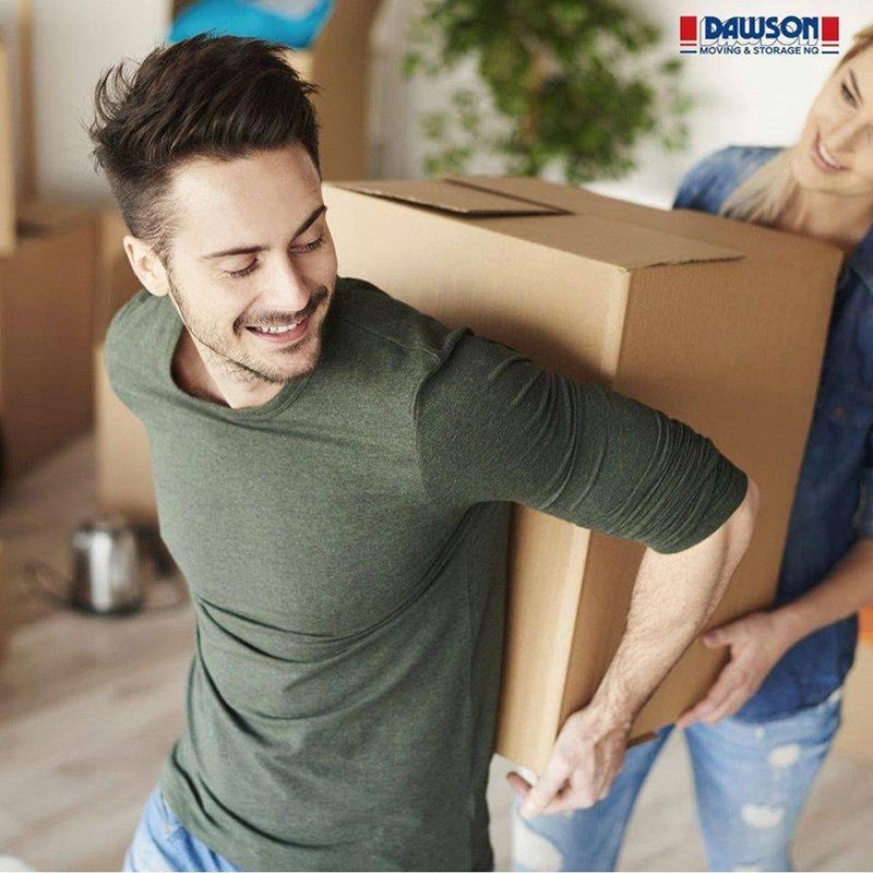 A Man Is Carrying A Large Cardboard Box While A Woman Holds It — Dawson Moving & Storage NQ in Mount St John, QLD
