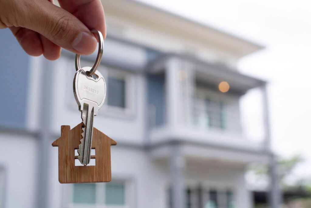 A Person Is Holding A Key With A House Keychain In Front Of A House — Dawson Moving & Storage NQ in Mount St John, QLD