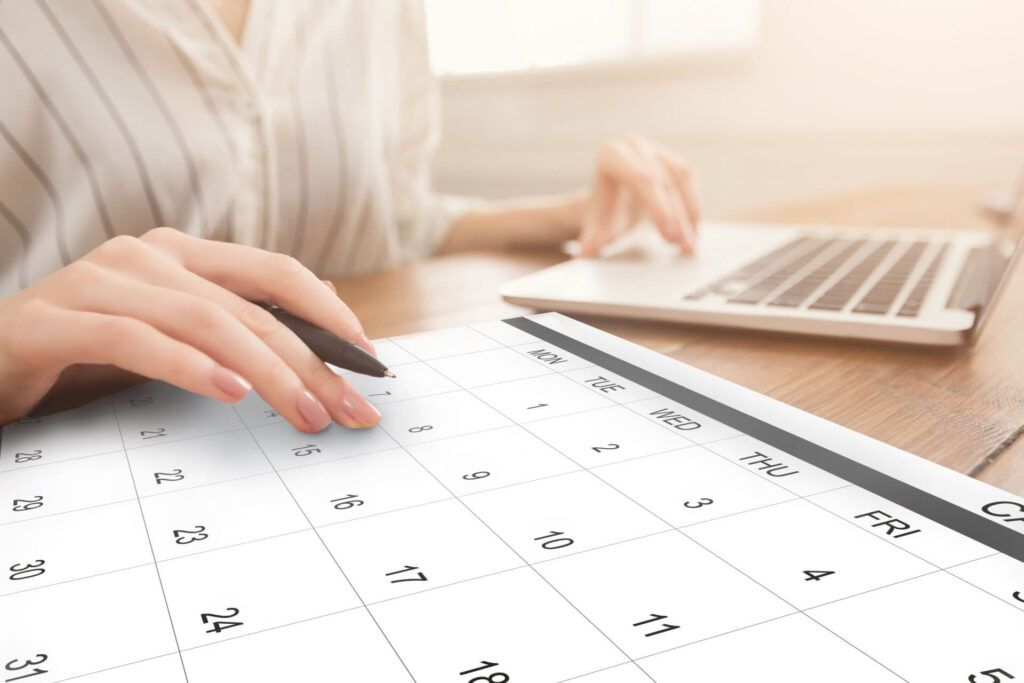 A Woman Is Sitting at A Table Using a Laptop and A Calendar — Dawson Moving & Storage NQ in Mount St John, QLD