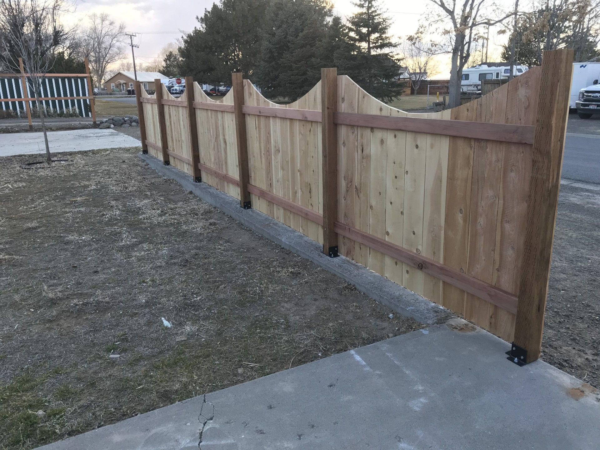A wooden fence is sitting next to a sidewalk in a yard.