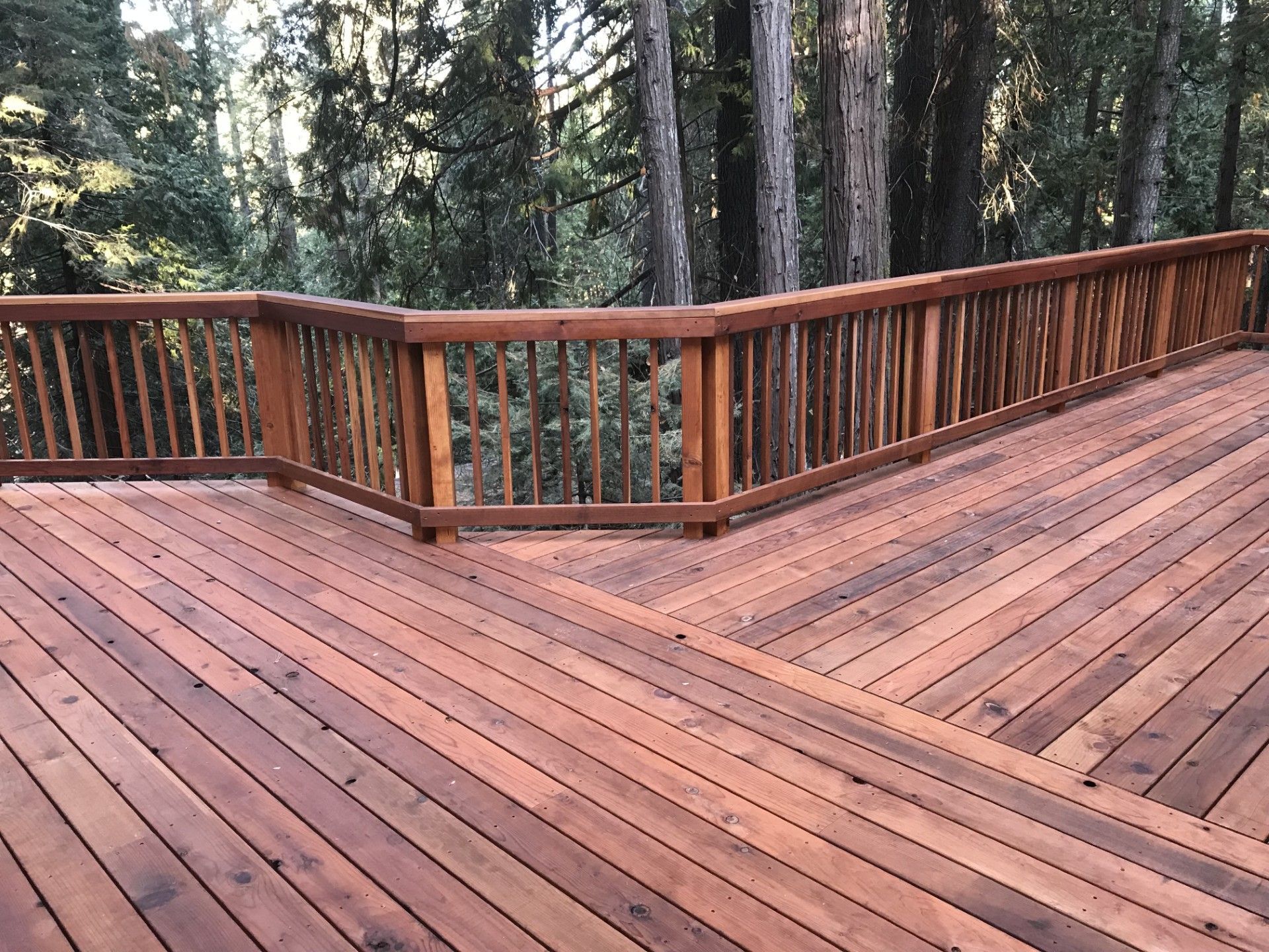 A wooden deck with a wooden railing and trees in the background