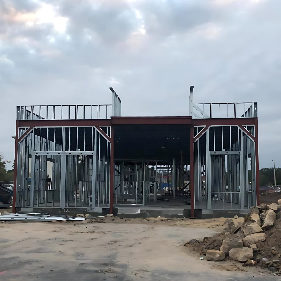 Steel frame of a building under construction, exterior view. Sky overhead; dirt and rocks in foreground.