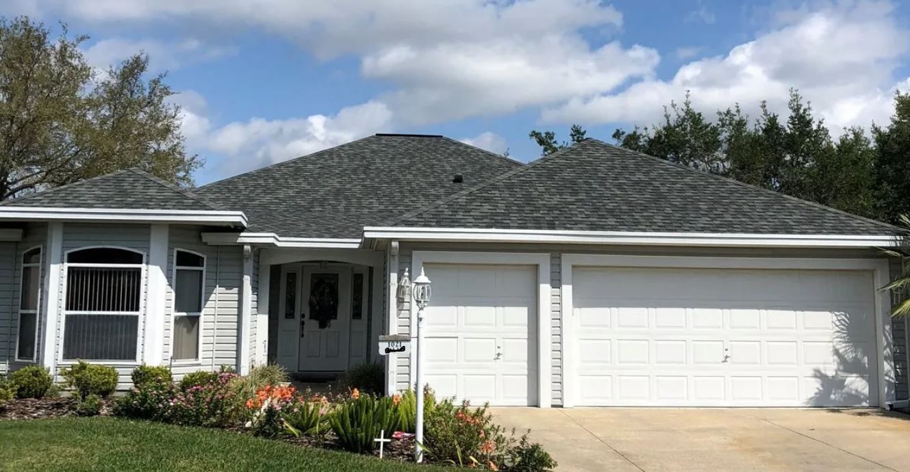 A white house with a gray roof and two garage doors.