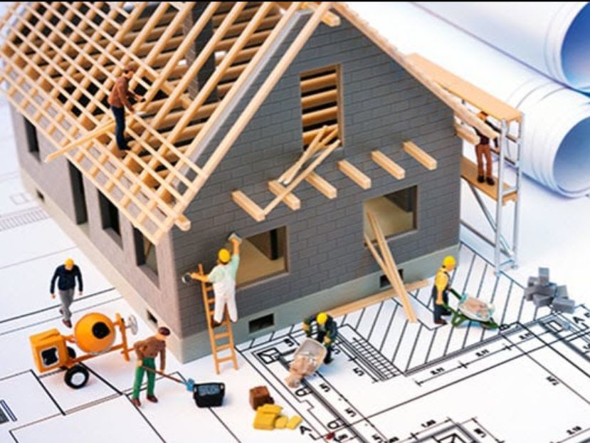 Miniature house under construction with workers, blueprints, and tools.