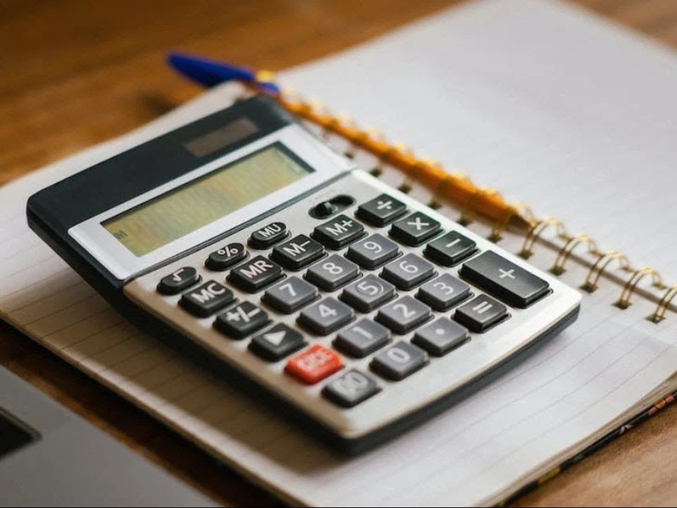 Calculator on open notebook with pen, on a wooden surface.