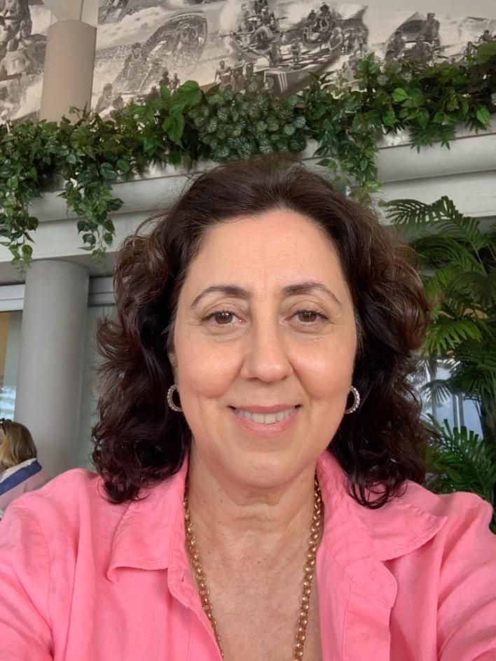 Woman in a purple dress and scarf holding a blue folder, smiling.