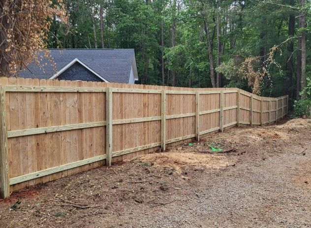 A wooden fence in Columbus Ga is sitting in the middle of a dirt field next to a house.