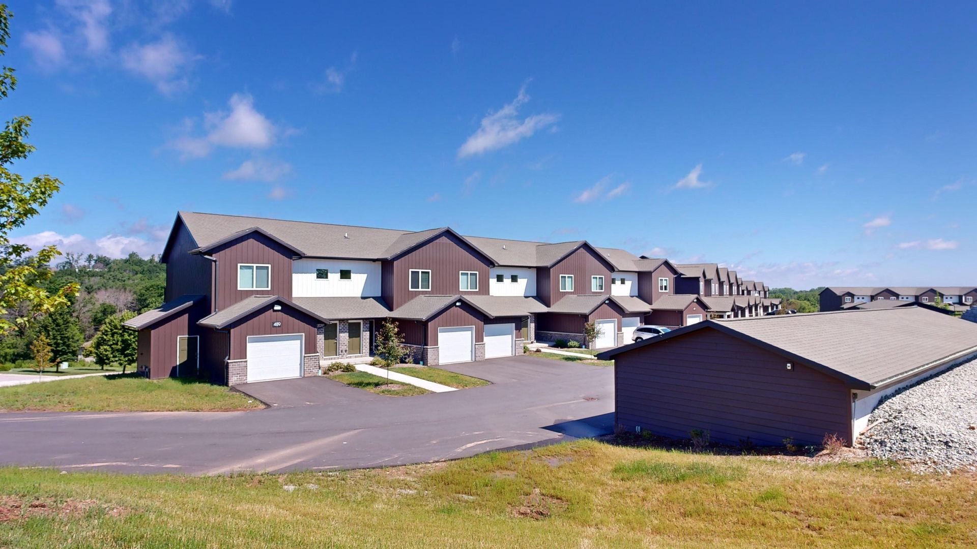 Suburban townhouse row with garages and a shed under a bright blue sky