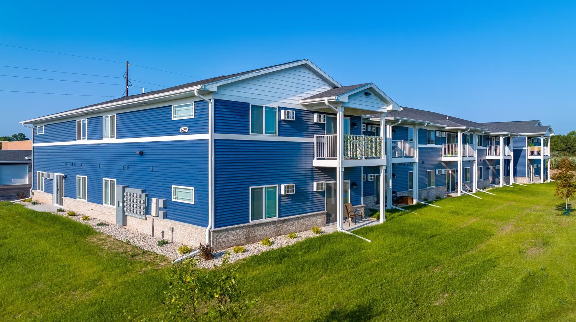Blue apartment building with white trim and balconies on a grassy lawn under a clear sky