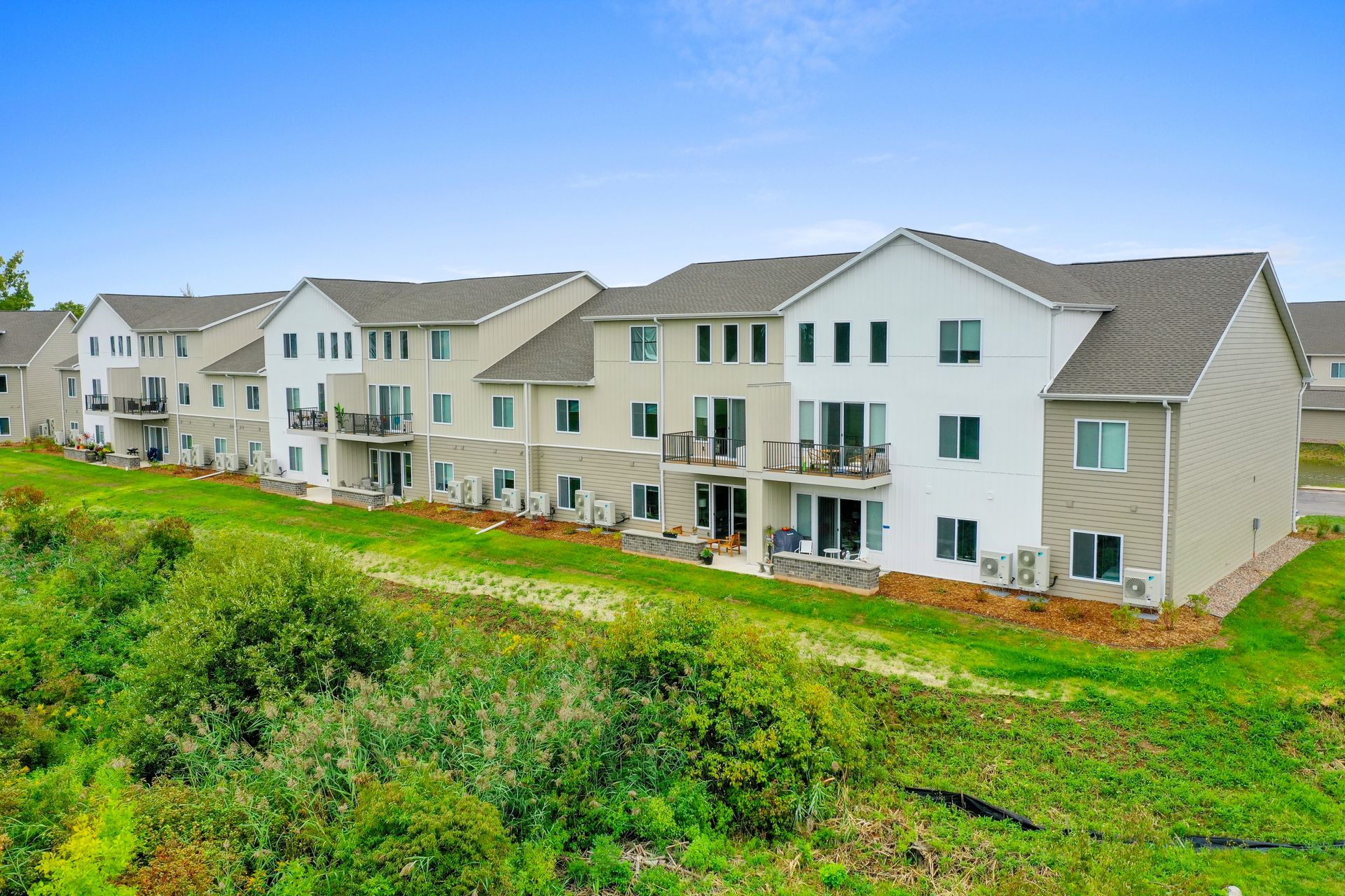 Row of new beige townhouses with green shutters beside a grassy hillside
