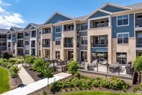 Modern apartment complex with balconies, landscaped walkway, and outdoor seating under a blue sky