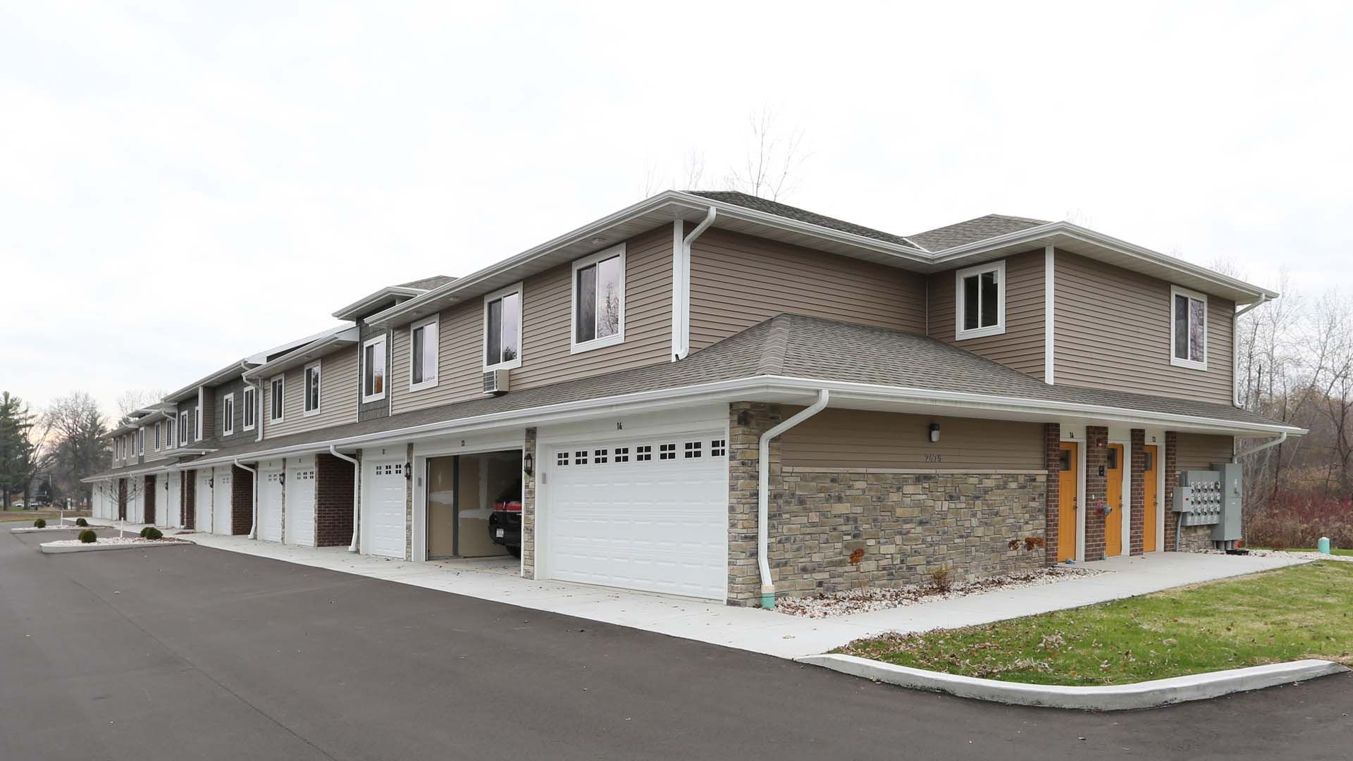 Row of modern townhomes with beige siding, stone accents, and attached garages along a quiet street