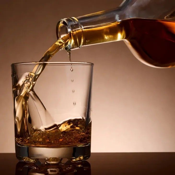 Whiskey being poured from a bottle into a rocks glass. Brown liquid, neutral background.