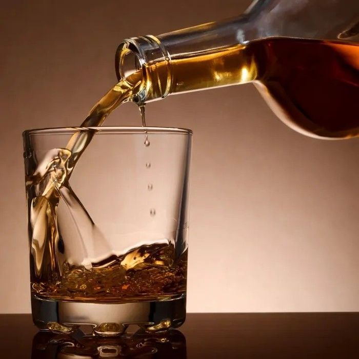 Whiskey being poured from a bottle into a glass, brown liquid, neutral background.