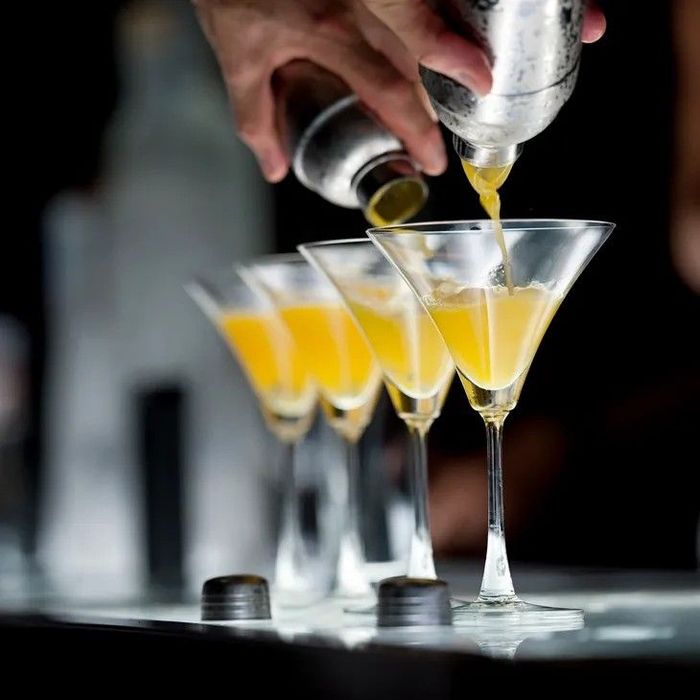 Bartender pouring yellow cocktail into glasses.