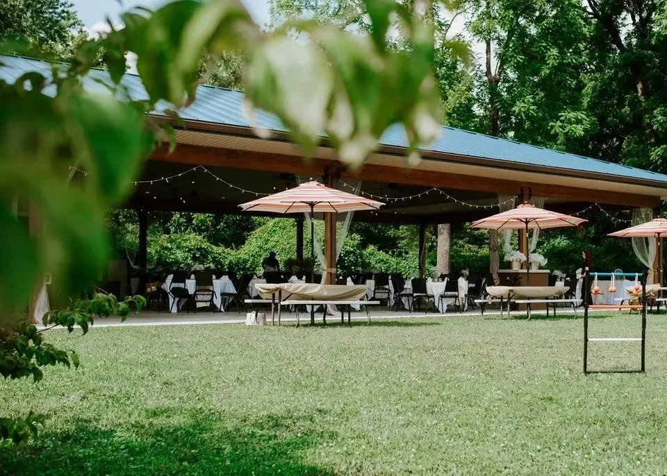 Outdoor event setup under a pavilion: tables with umbrellas on green grass.