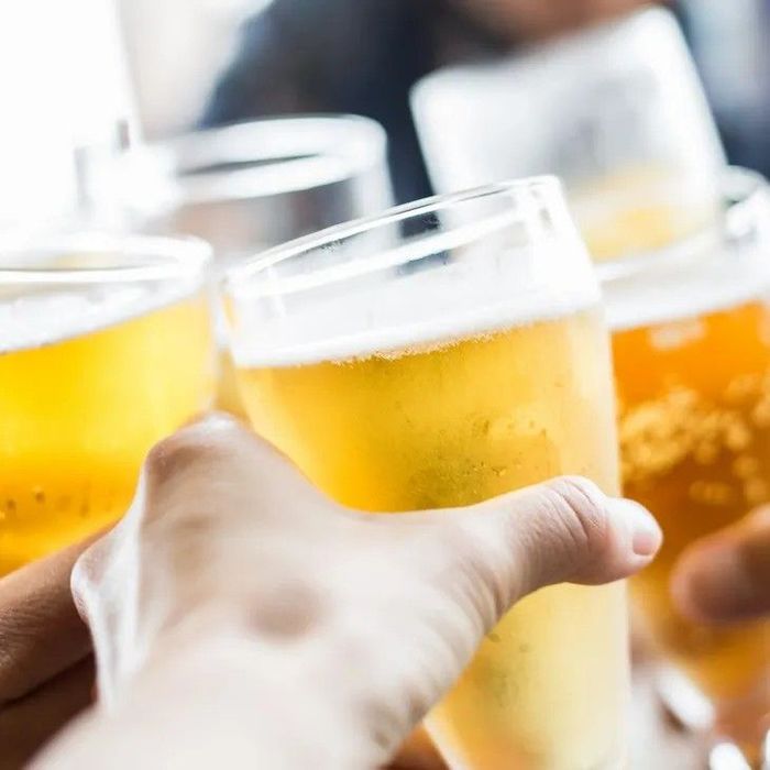 Hands clinking beer glasses in a toast. Light yellow beer with foam, close-up.