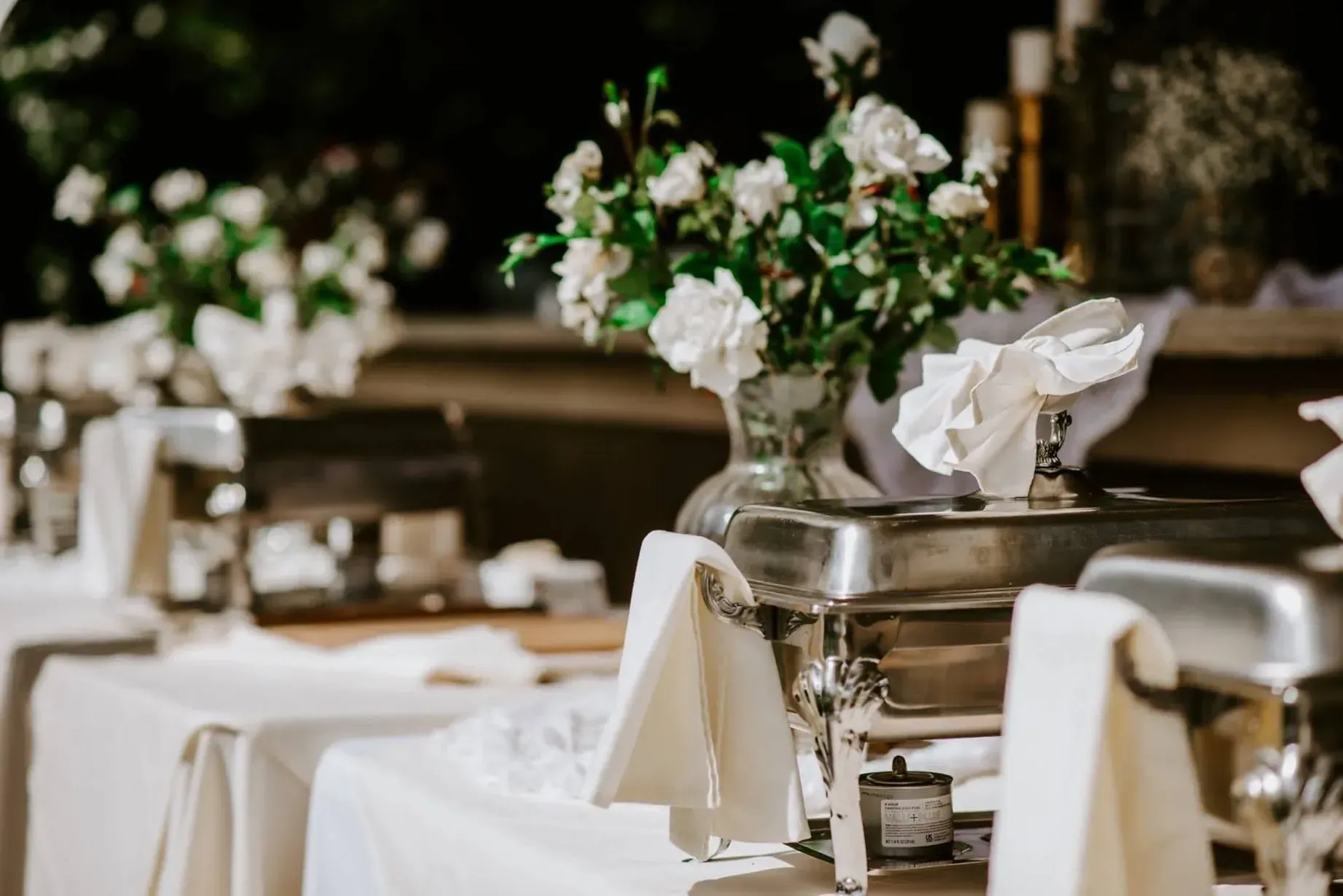 Buffet tables set with white linens, stainless steel chafing dishes, and floral centerpieces.