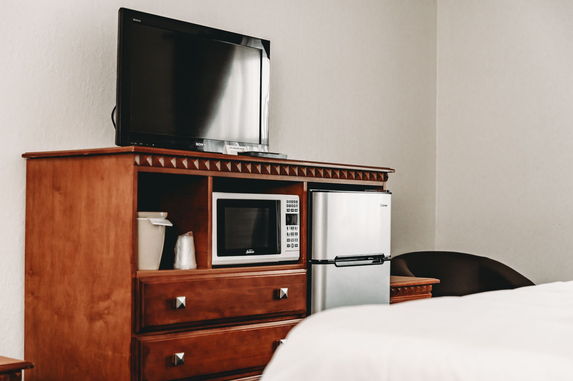 Wooden cabinet with a TV, microwave, mini-fridge, and drawers in a bedroom.