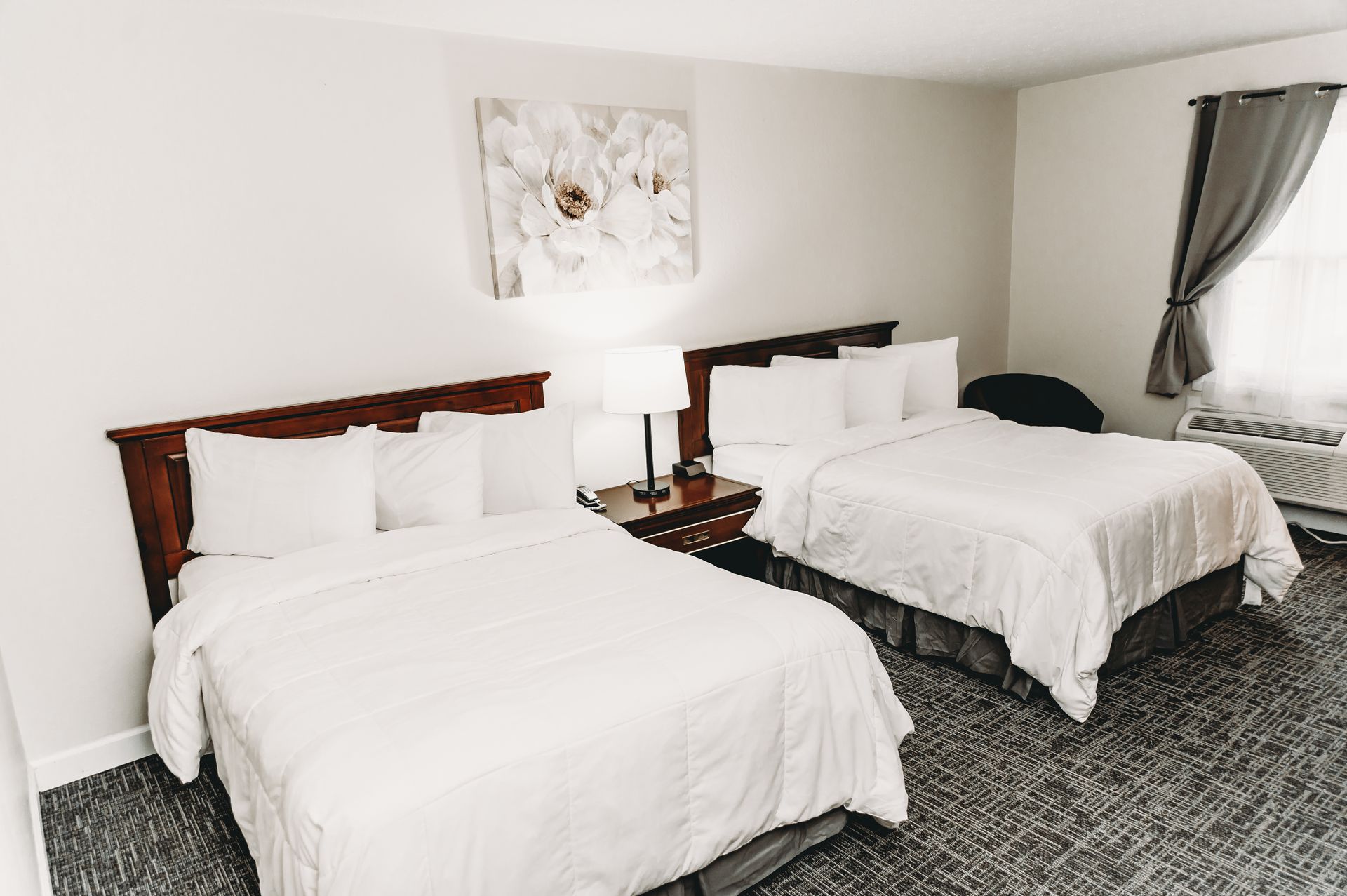 Hotel room with two queen beds, white bedding, dark wood headboards, and a lamp on a nightstand.