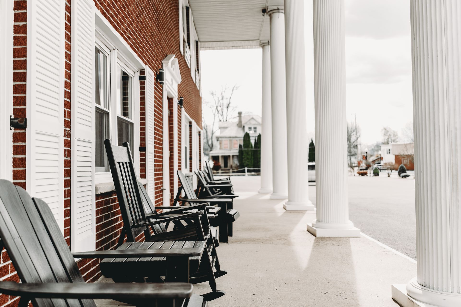 A brick building with white columns and shutters; blue chairs on a porch.