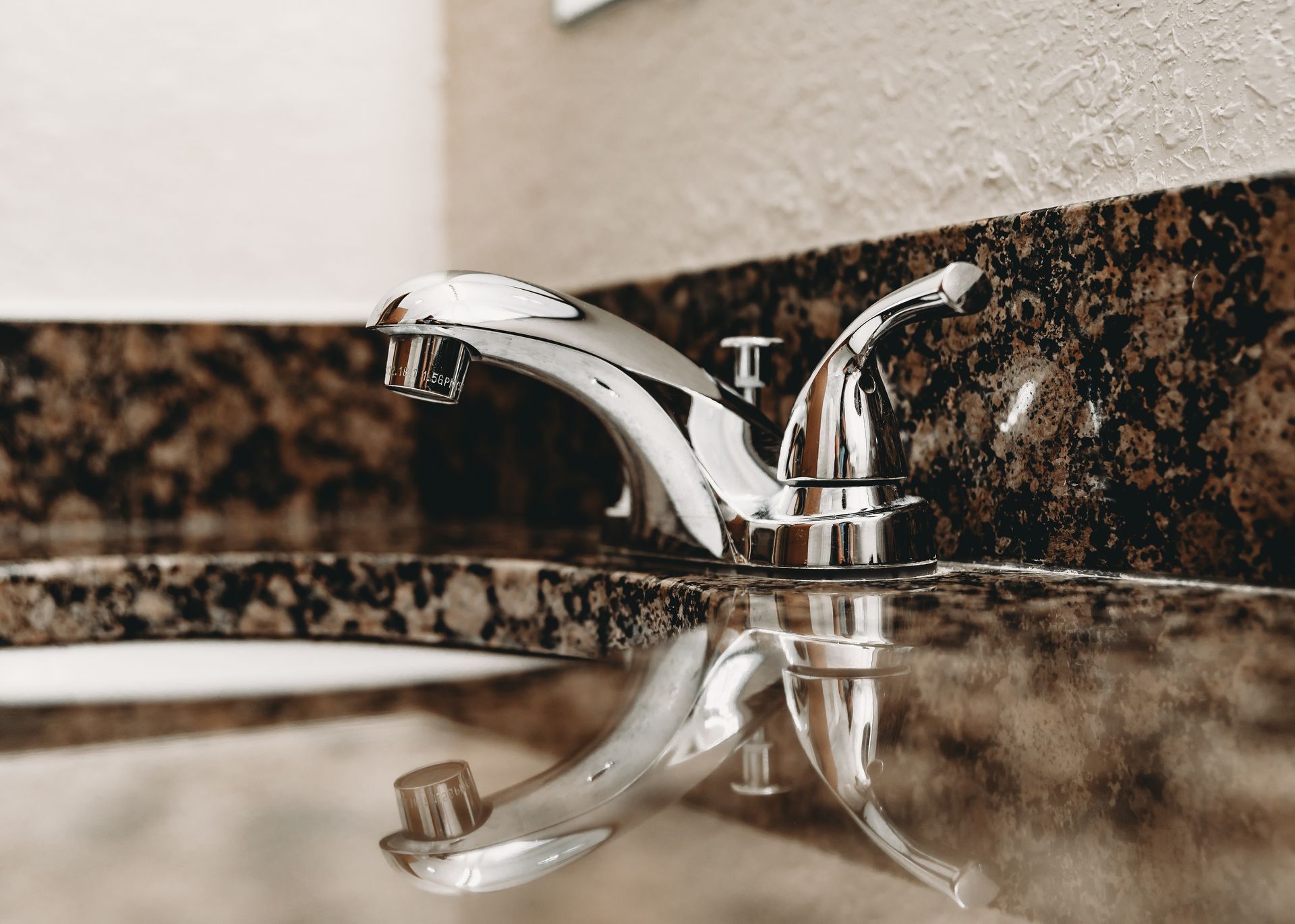 Chrome faucet on a brown and black speckled countertop, with a reflection of the faucet visible.
