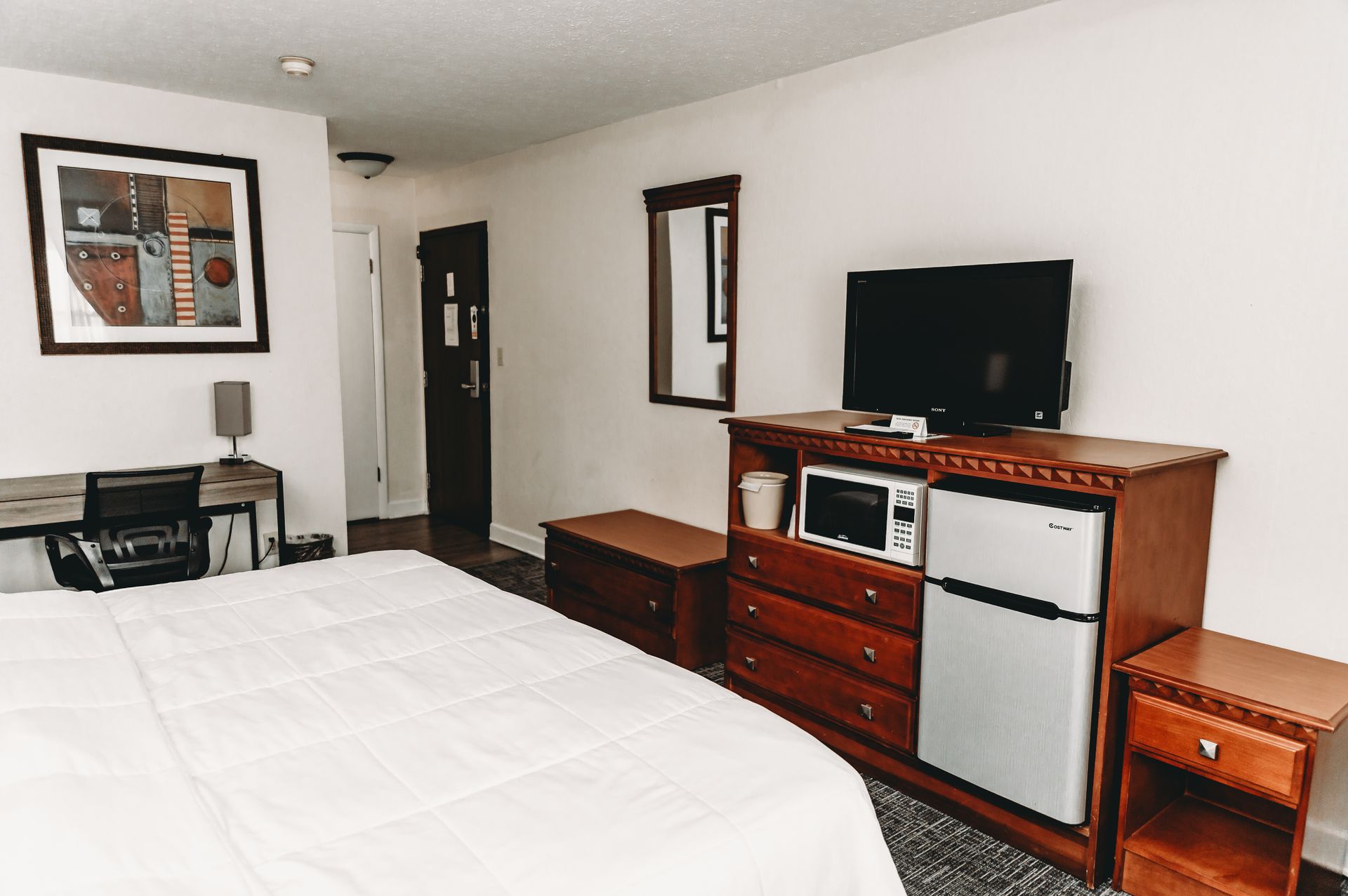 Hotel room with bed, desk, TV, microwave, mini-fridge, and mirror.